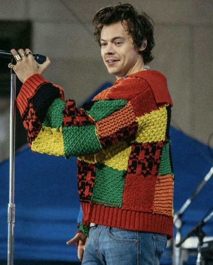 a man standing on top of a stage holding a microphone in his right hand and wearing a multicolored sweater