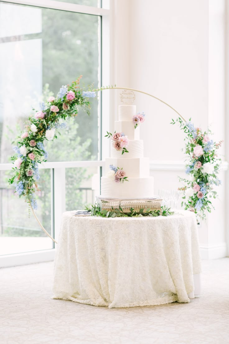 a white wedding cake sitting on top of a table next to a tall glass window