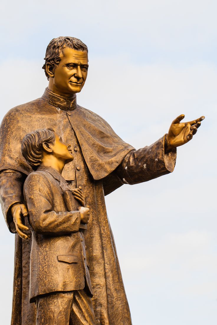 a statue of a man holding a young child in his arms with the sky behind him