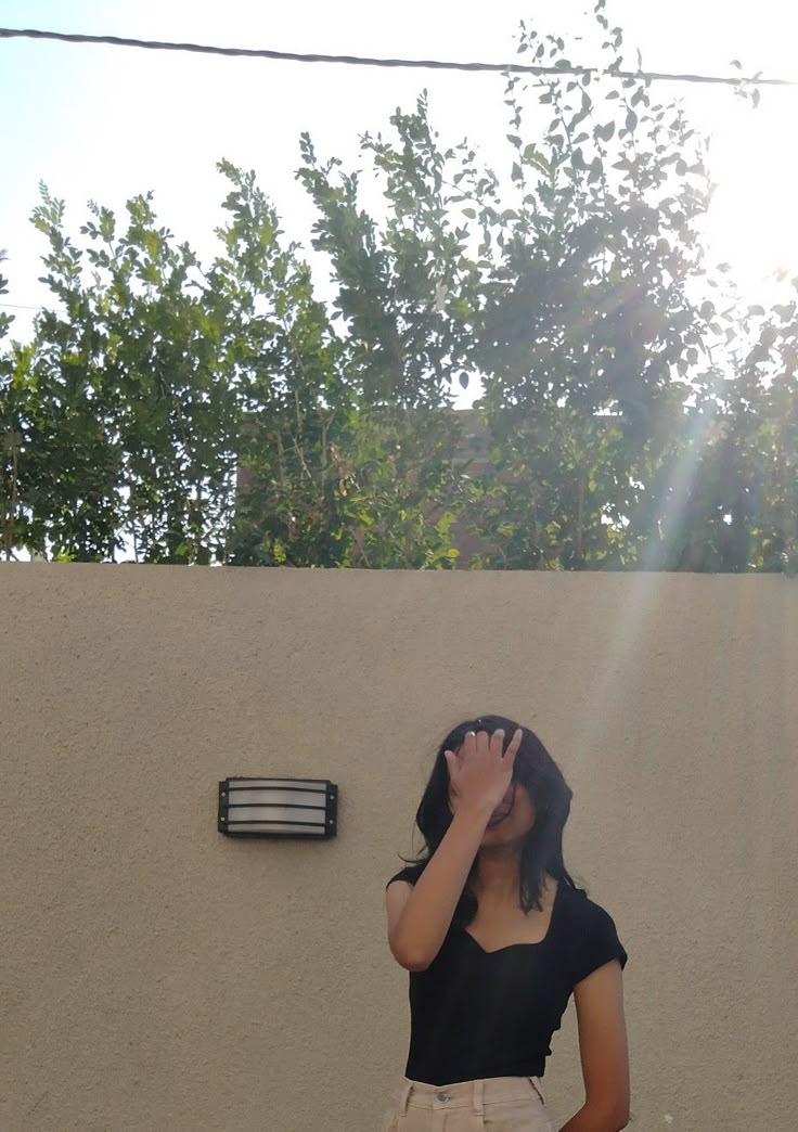 a woman standing in front of a wall covering her eyes