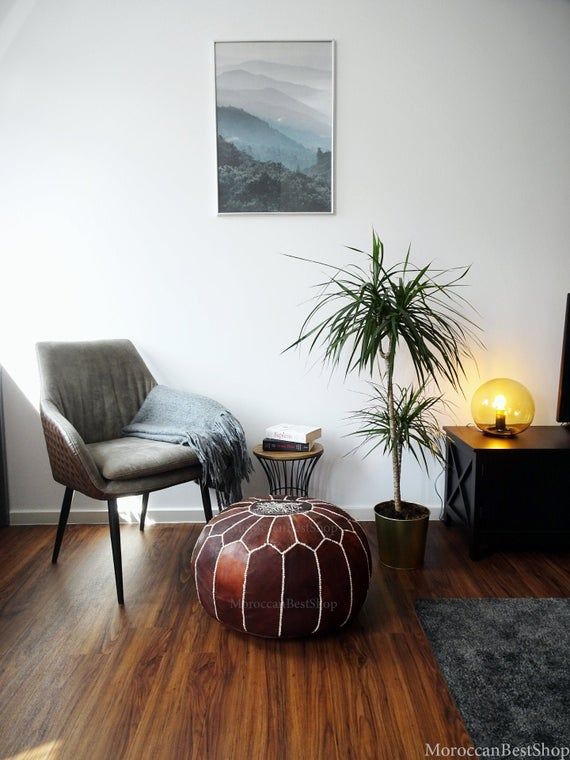 a living room with a chair, ottoman and potted plant on the floor in front of it