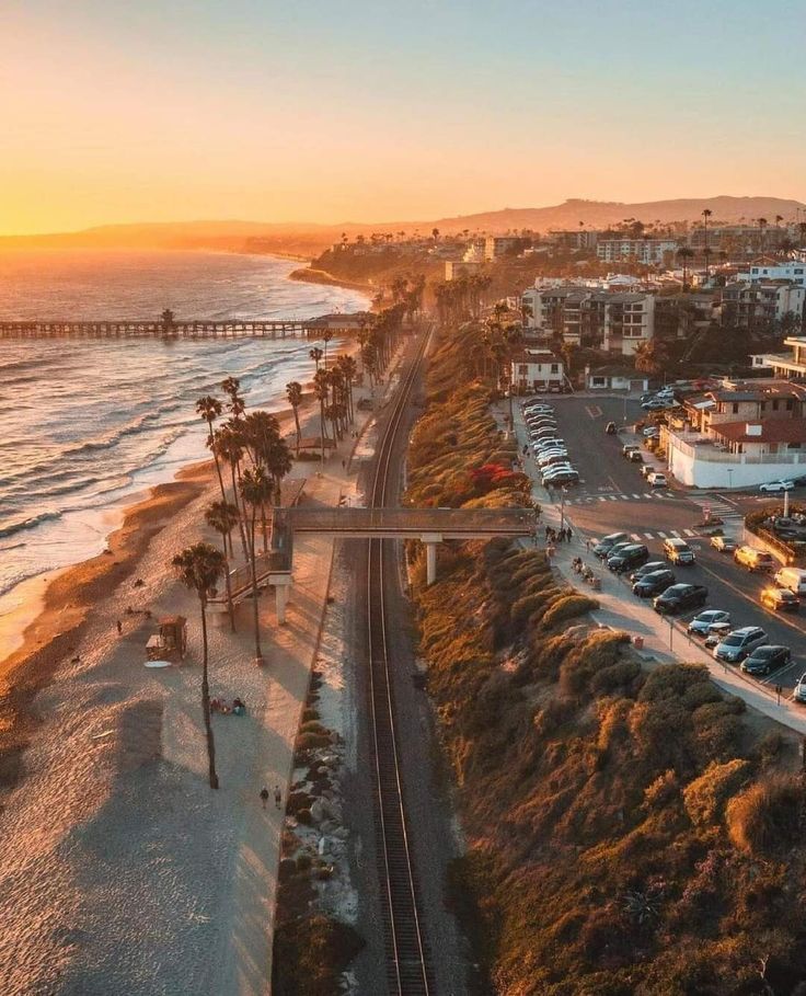 an aerial view of the beach and ocean with cars parked on the road next to it