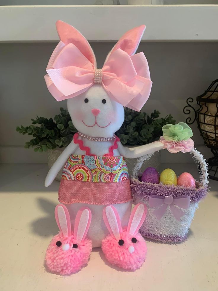 a stuffed bunny holding a basket with easter eggs in it's paws and wearing a pink bow