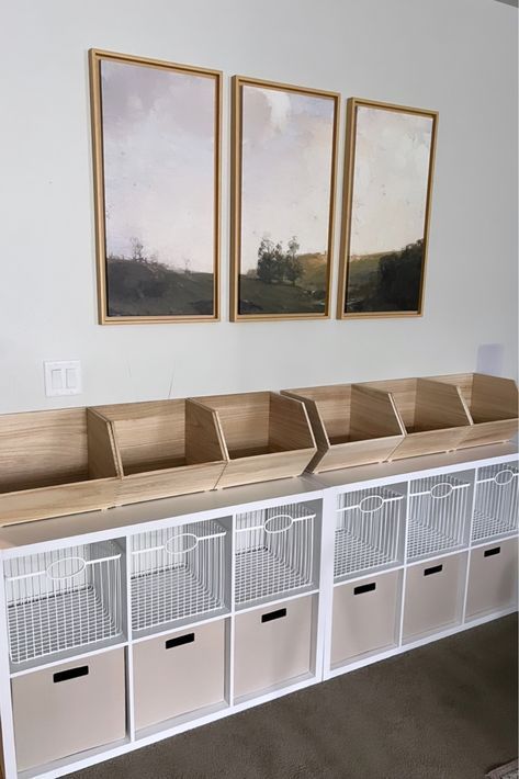 three pictures hang on the wall above white storage bins with drawers and baskets underneath them