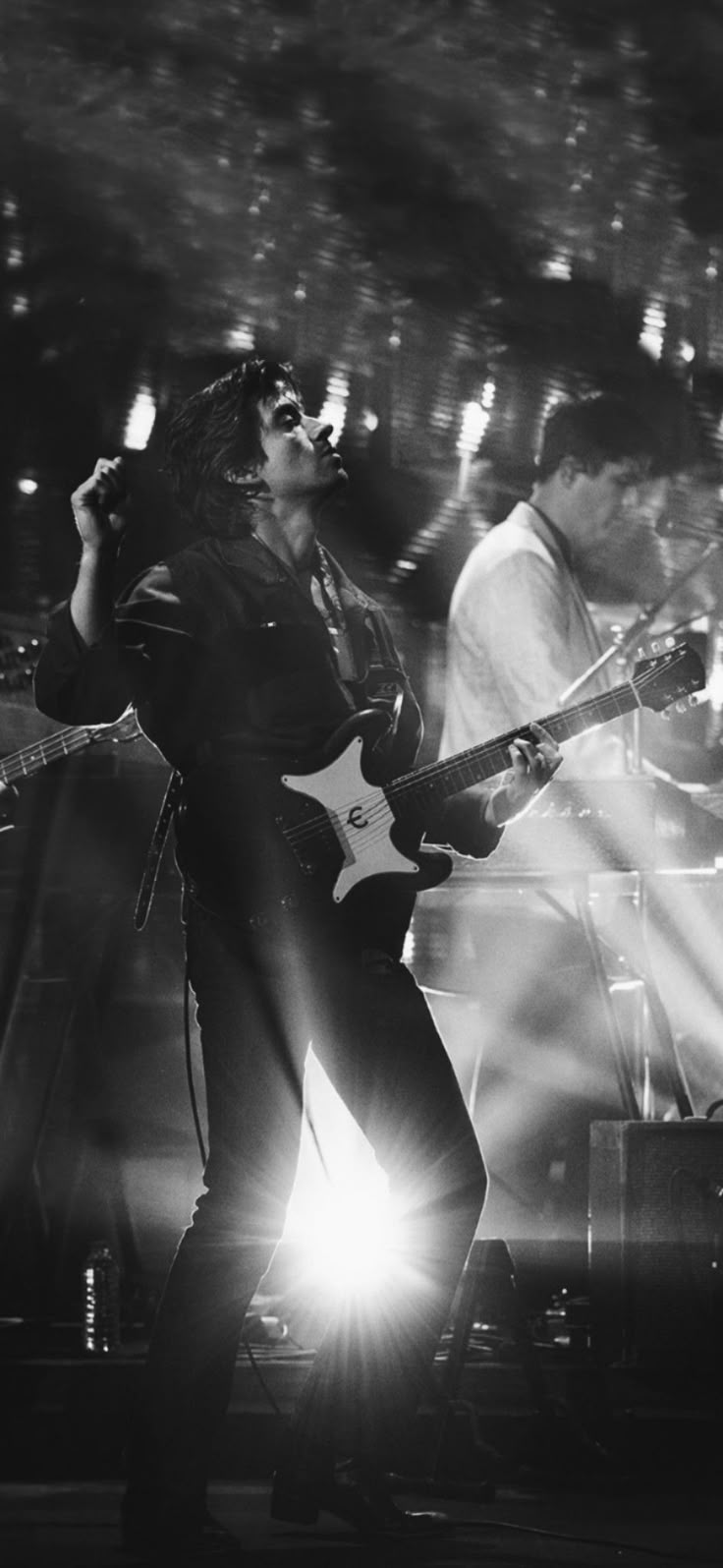 black and white photo of band performing on stage with lights shining down from behind them