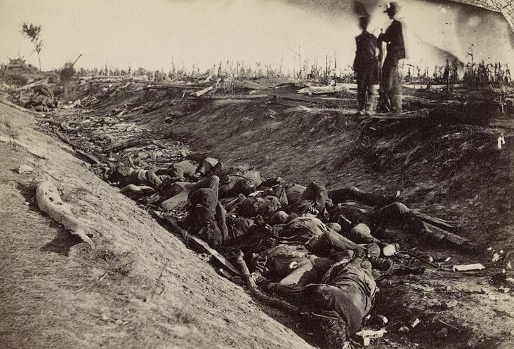 an old black and white photo of men standing on top of a hill with dead bodies