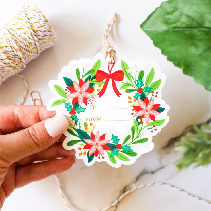 a hand holding a christmas ornament with holly and poinsettis on it