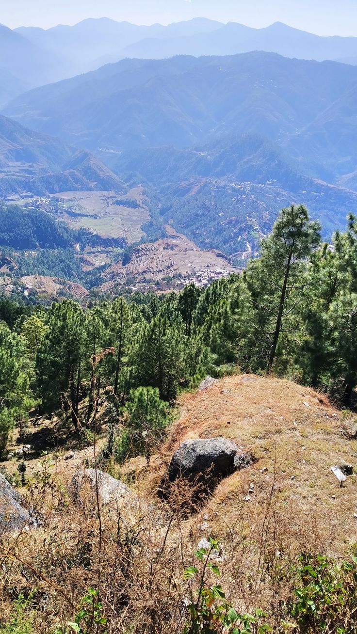 a mountain view with trees and mountains in the backgrouund, looking down into the valley below