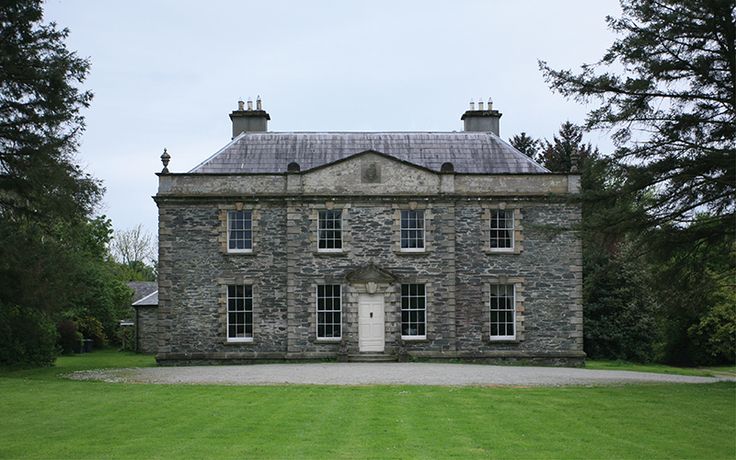 an old stone house with two chimneys on the top and one at the bottom, surrounded by green grass