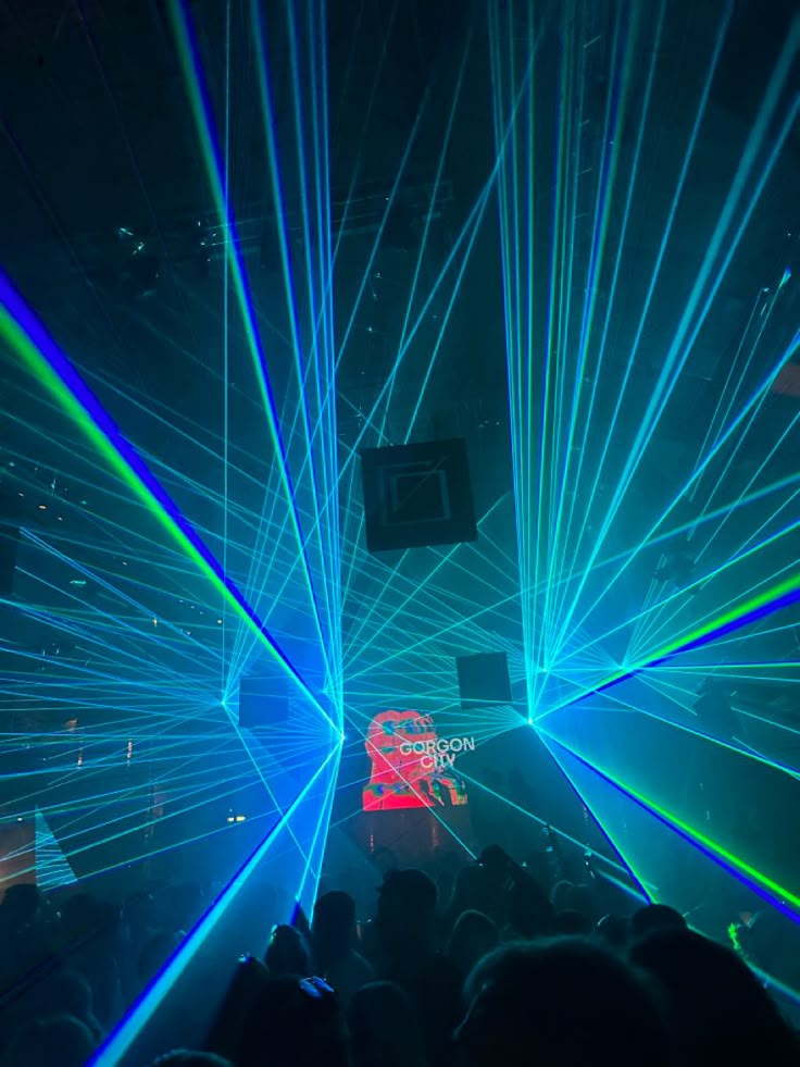 a large group of people at a concert with laser lights on their faces and hands in the air