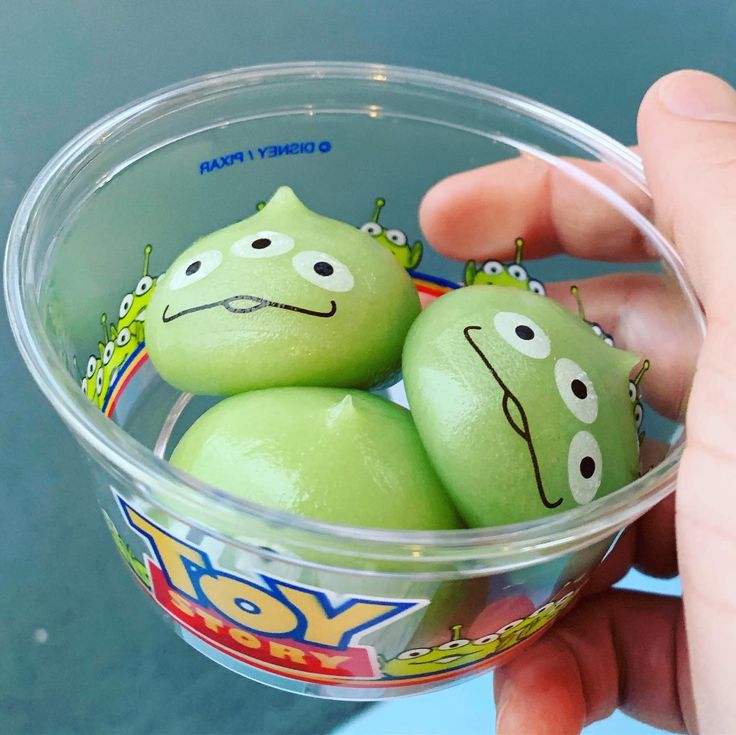 a person holding a plastic cup filled with green eggs covered in googly eyes and faces