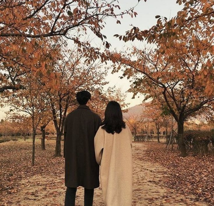 a man and woman walking down a path in the fall