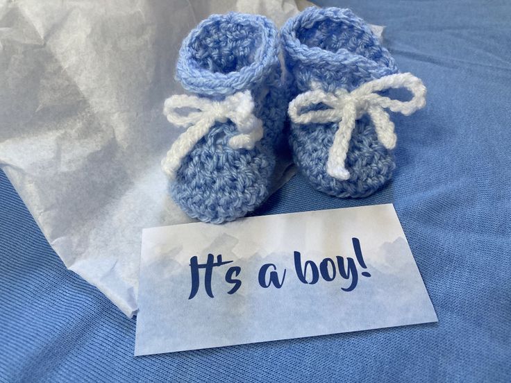 a pair of blue baby booties sitting on top of a bed next to a sign