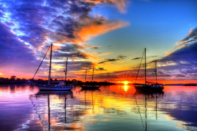 several sailboats floating in the water at sunset