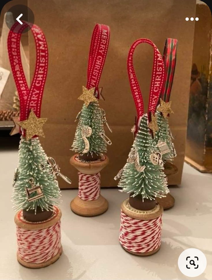 three small christmas trees sitting on top of twine spools with ribbons around them