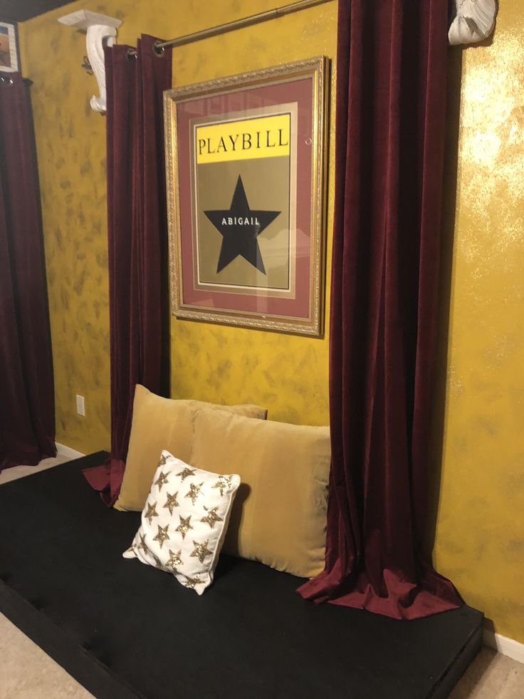 there is a bed with red curtains and a black pillow in front of the yellow wall