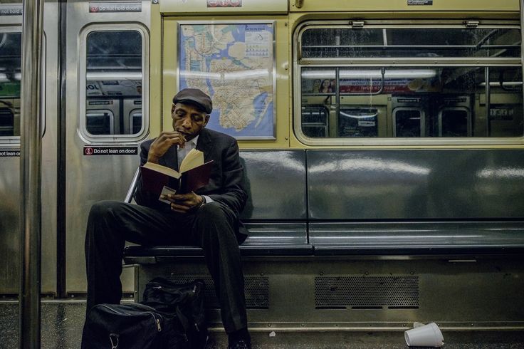 a man sitting on a subway bench reading a book