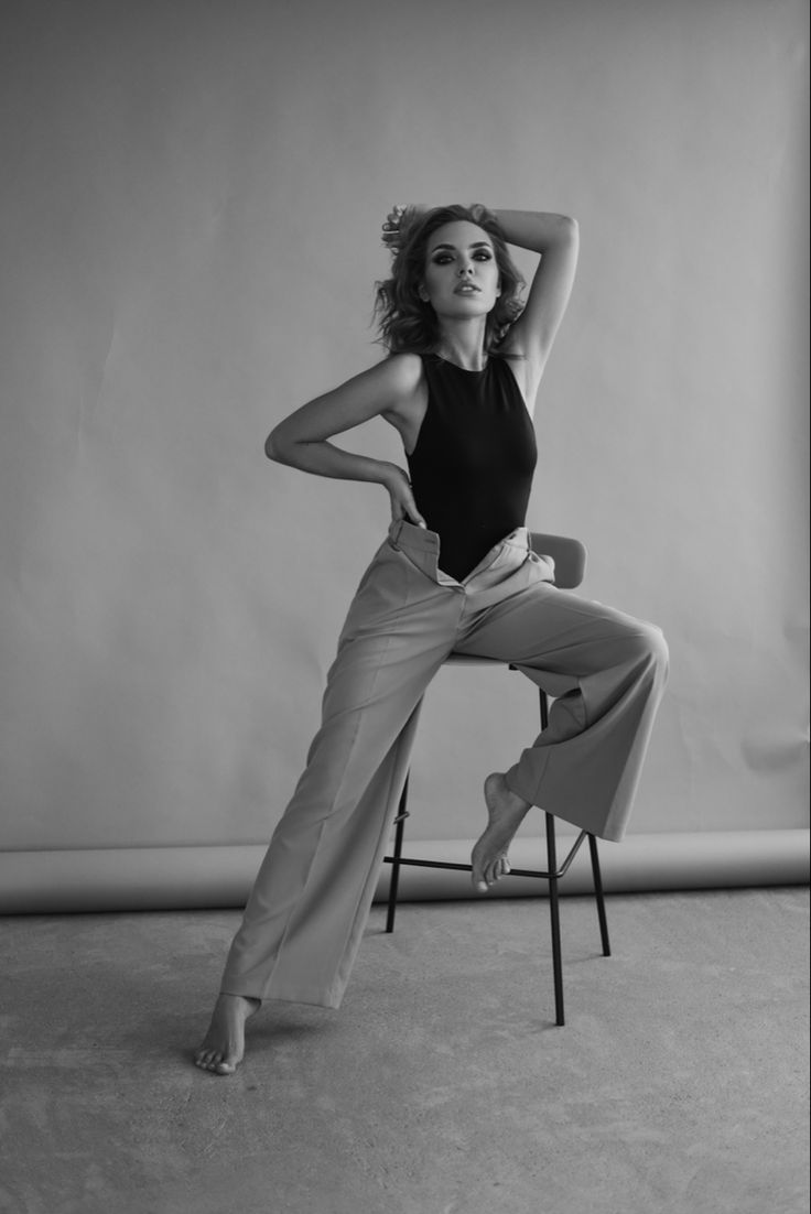 black and white photograph of woman sitting on chair with arms behind her head, leaning forward