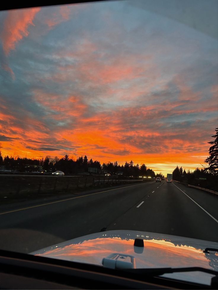 the sun is setting on an empty road with trees in the distance and clouds in the sky