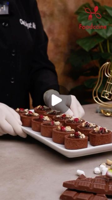 a person in white gloves is serving desserts on a platter with chocolate and nuts