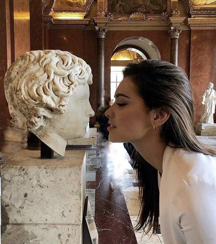 a woman is kissing a bust of a man in a room with marble sculptures on the walls