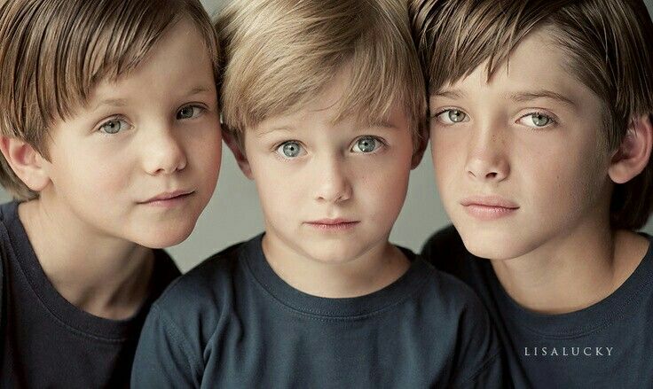 three young boys standing next to each other in front of a gray background with one boy looking at the camera