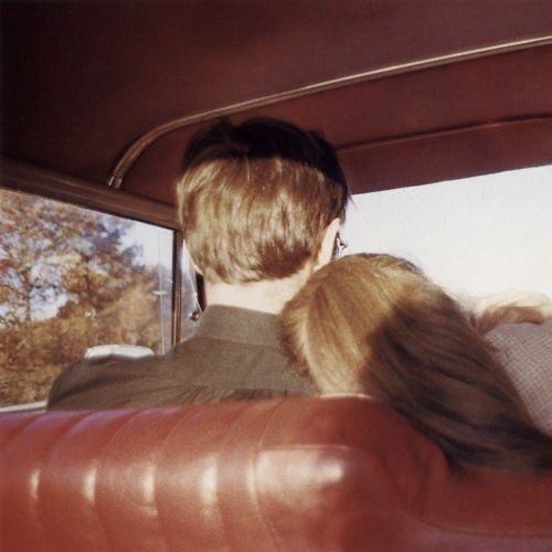 two people sitting in the back seat of a car looking out the window at trees