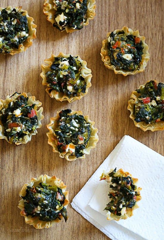 small tarts filled with spinach and cheese on top of a wooden table next to a white napkin