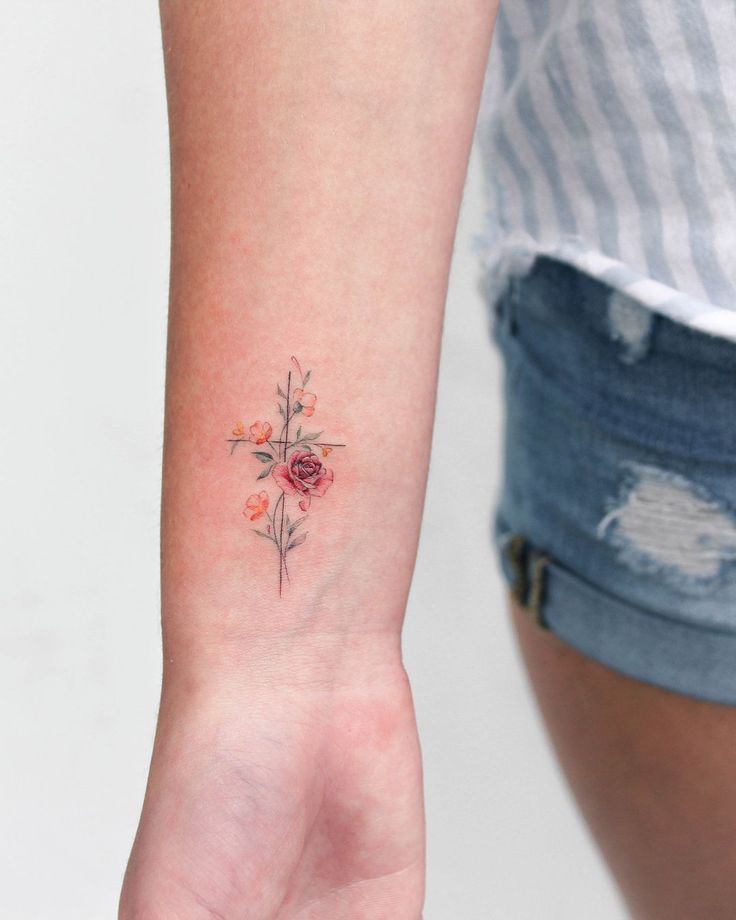 a woman's arm with a small cross and flowers tattoo on the left wrist