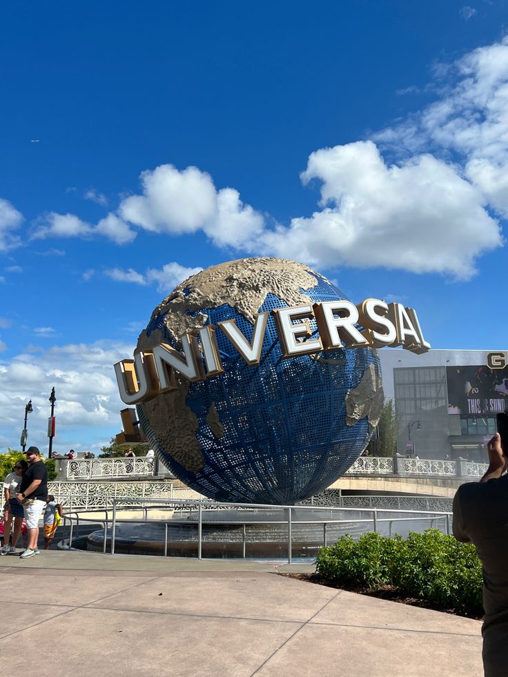 people are standing in front of the universal studios sign with a blue sky and clouds behind them