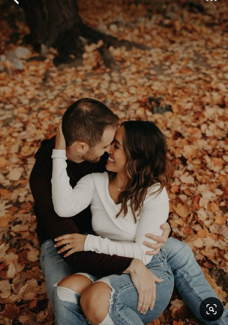 a man and woman are sitting on the ground surrounded by leaves with their arms around each other