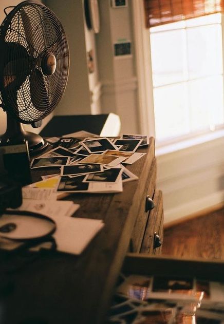 an old fan sitting on top of a wooden table in front of a window filled with pictures