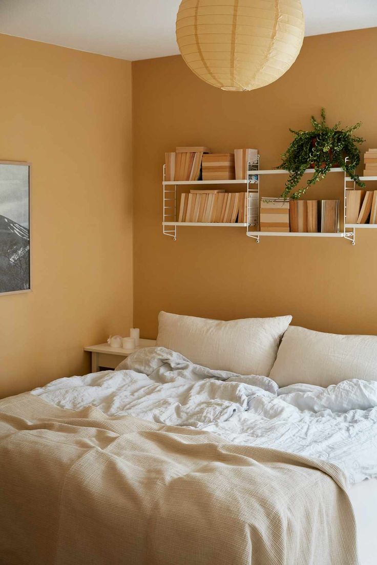 an unmade bed in a bedroom with bookshelves on the wall above it