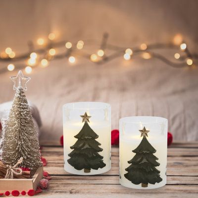 two lit candles sitting next to each other on a wooden table with christmas decorations around them