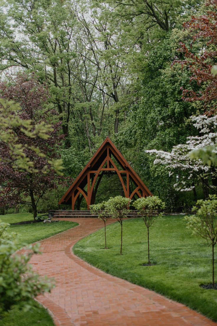 a wooden structure sitting in the middle of a lush green park next to a brick path