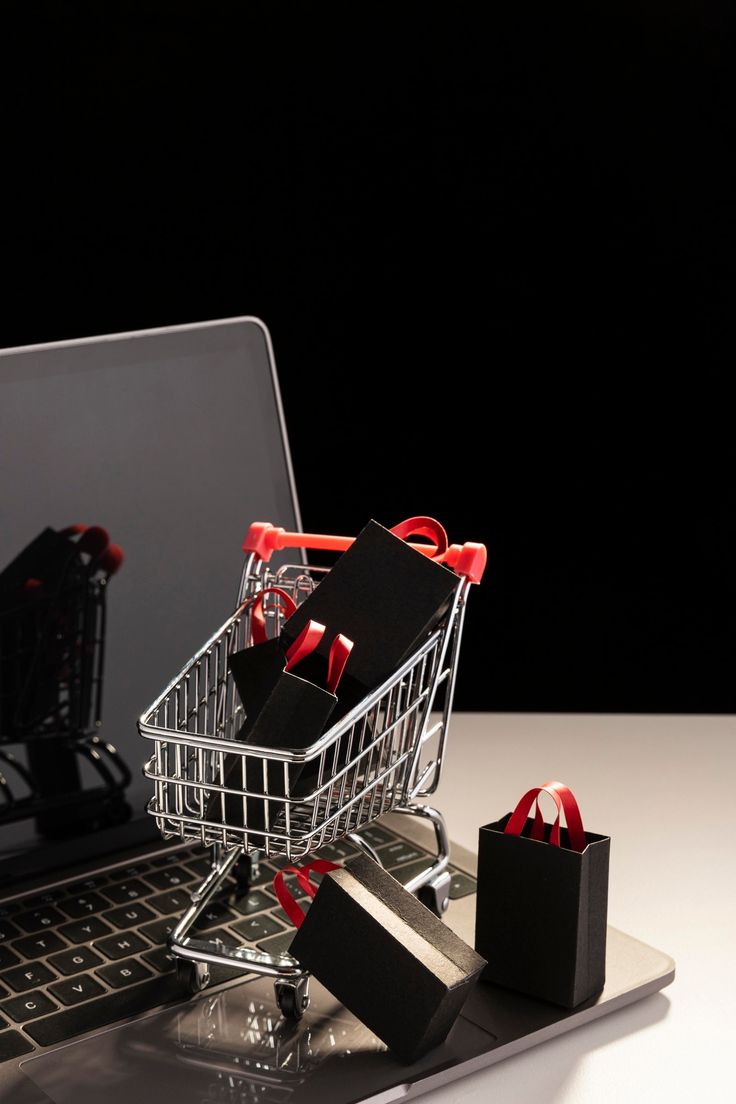 a shopping cart sitting on top of a laptop computer next to some small black bags