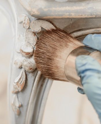 a person in blue gloves is painting a white chair with gold paint and a brush