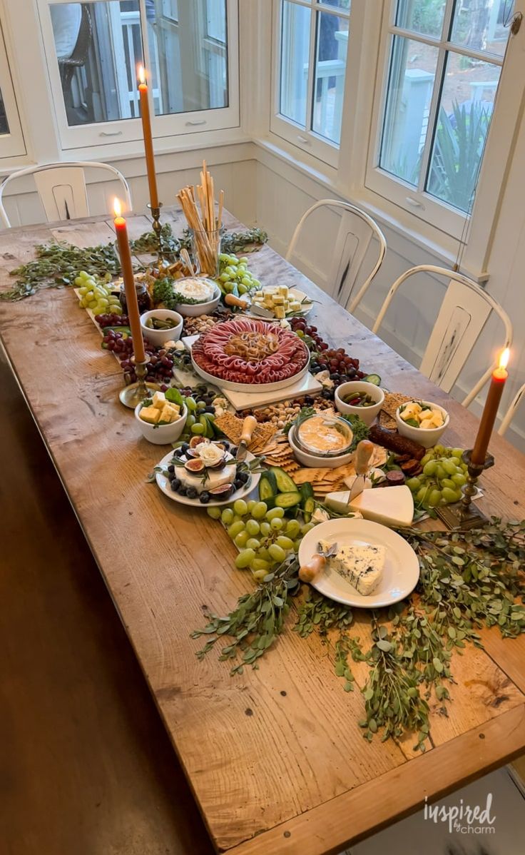 a wooden table topped with lots of plates and bowls filled with food next to candles