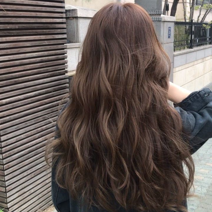 the back of a woman's head with long, wavy brown hair in front of a building