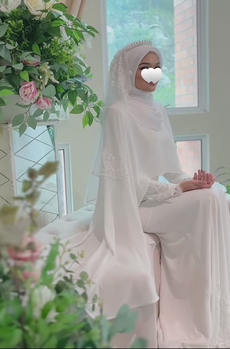 a woman wearing a white veil sitting in front of a vase with flowers on it