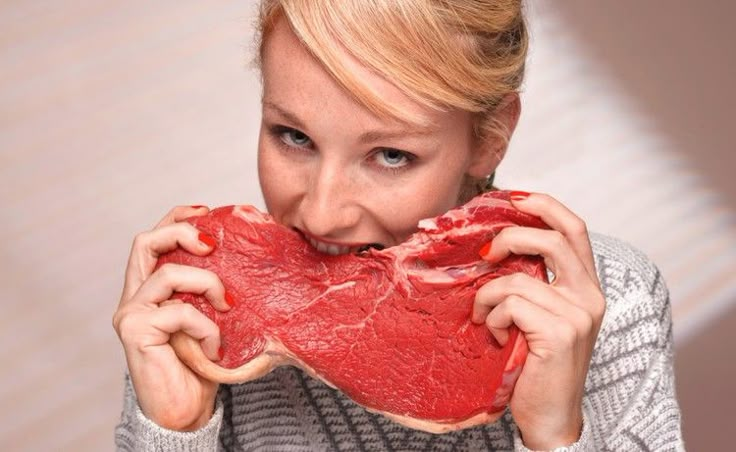 a woman holding up a piece of meat to her face and looking at the camera