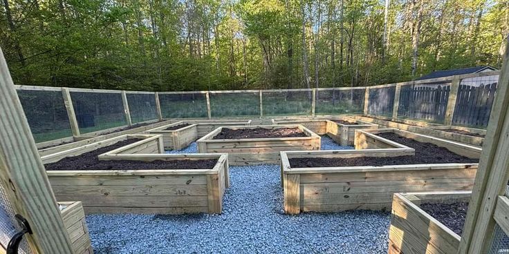 an outdoor vegetable garden with raised beds and gravel in the middle, surrounded by trees