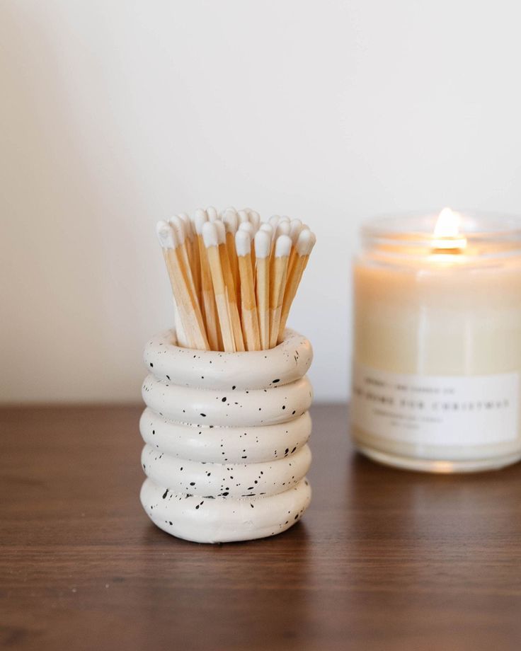 a candle and some matches sitting on a table next to a white container with black speckles