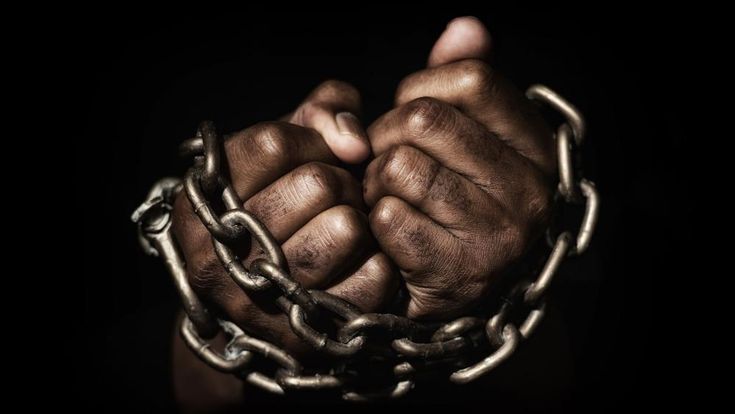 two hands holding chains in the dark with one hand on top of another, while the other is chained