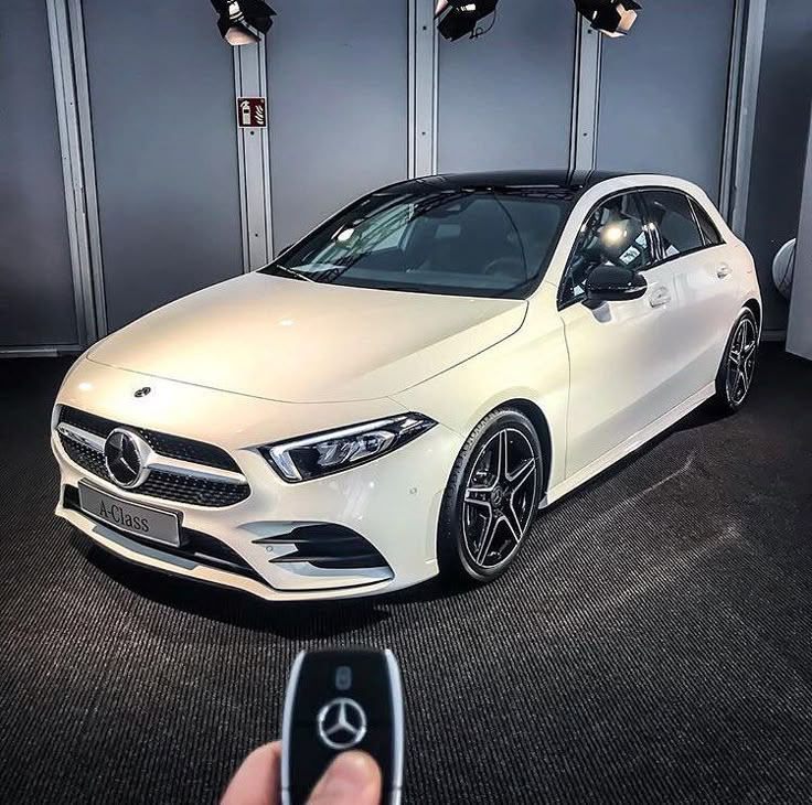 a person holding a remote control in front of a white mercedes cla car on display