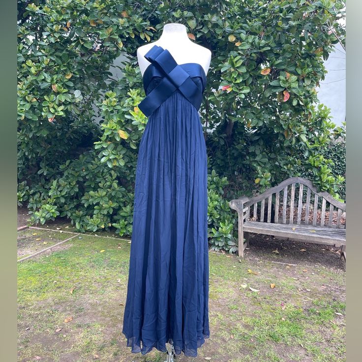 a blue dress is on display in front of some bushes and a bench with an apple tree behind it