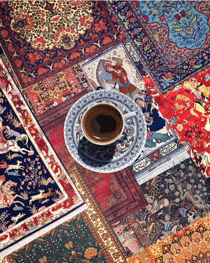 a cup of coffee sitting on top of a table surrounded by rugs and carpets