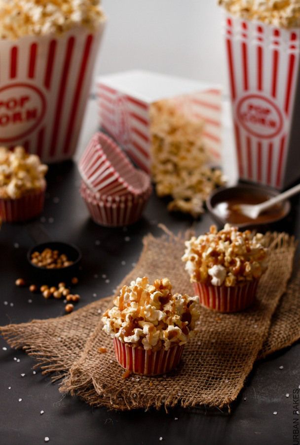 three red and white striped popcorn cups on a black surface with spoons next to them