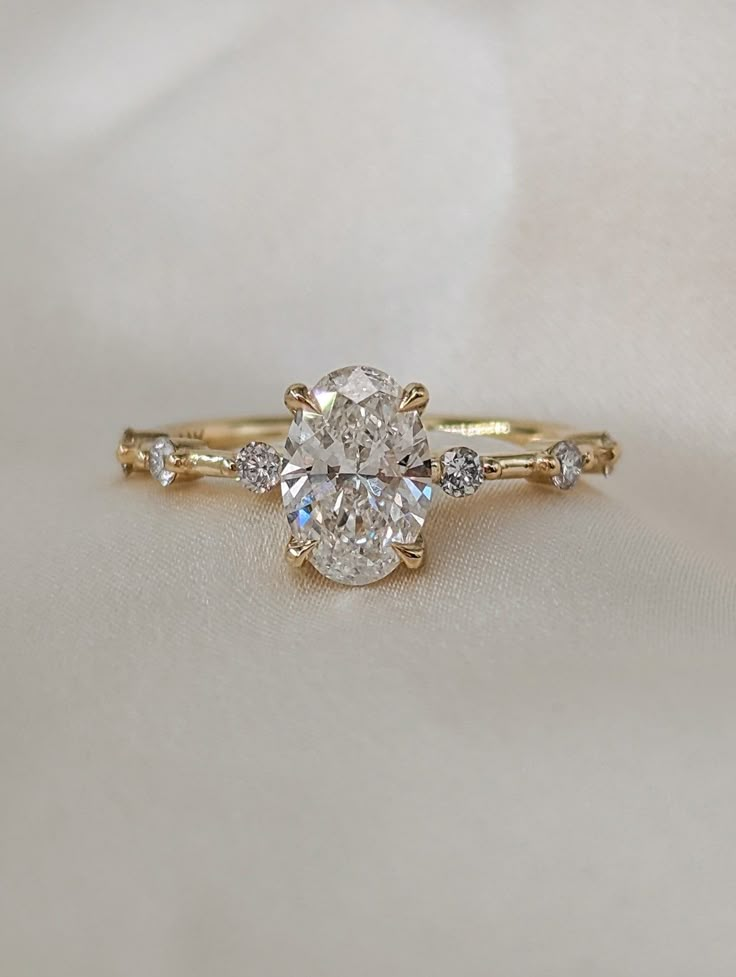 a close up of a diamond ring on a white cloth with gold band and side stones