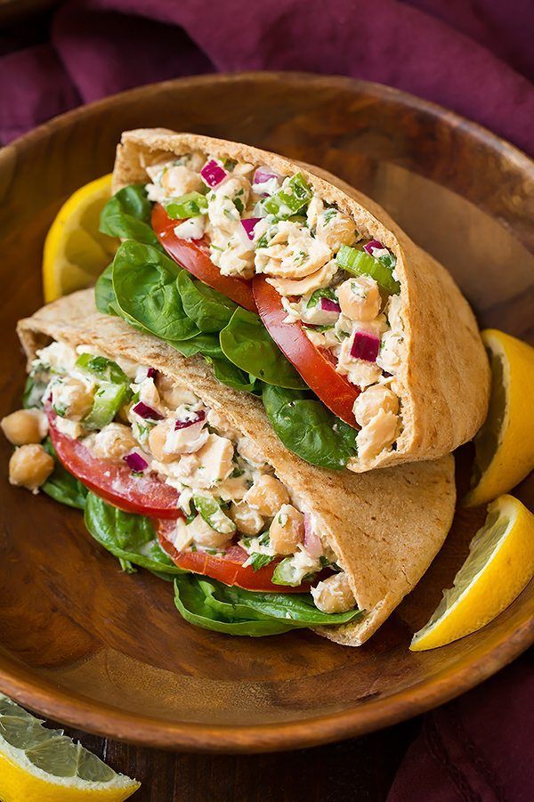 two wraps filled with chicken, lettuce and tomatoes on top of a wooden plate